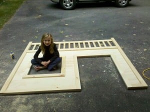 a little girl sitting on a driveway on a piece of plywood