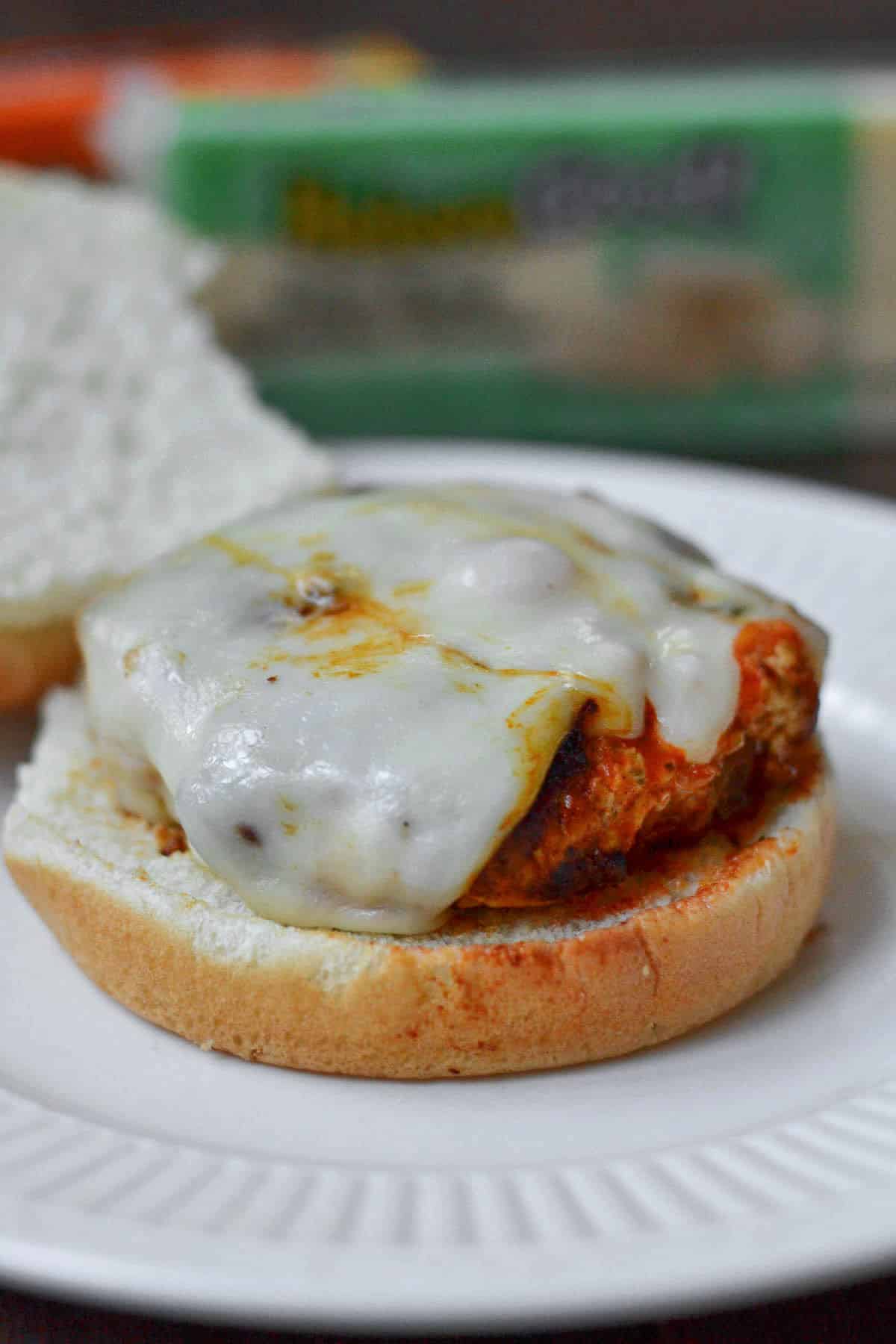 closeup of a Buffalo Turkey Burger recipe topped with melted cheese on a white plate
