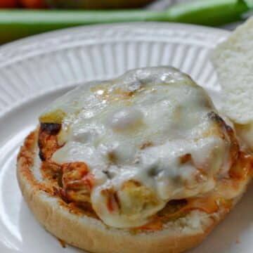 Buffalo Turkey Burger topped with melted cheese on a white plate with celery in background