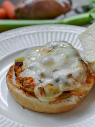 Buffalo Turkey Burger topped with melted cheese on a white plate with celery in background