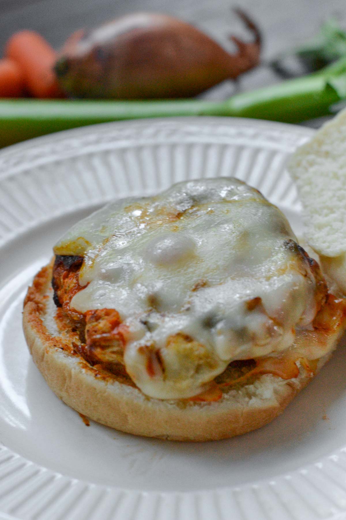 Buffalo Turkey Burger topped with melted cheese on a white plate with celery in background