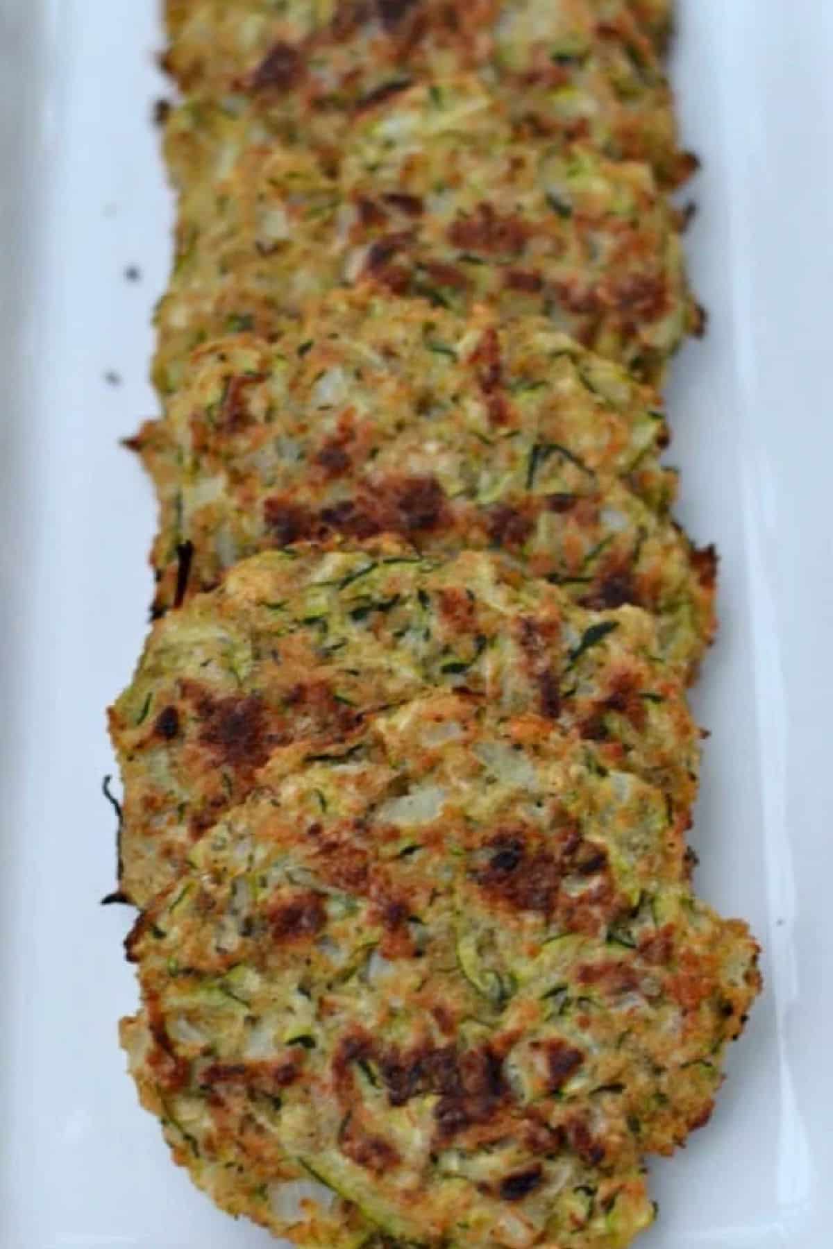 Baked Zucchini Cakes are a much healthier option to fried with the same crispiness. So quick to make and loaded with flavor, they are a great new way to serve this favorite veggie. Baked Zucchini Cakes on a white plate