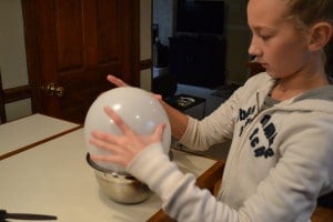 a girl holding a white balloon over a bowl