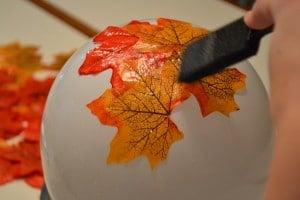 glueing fake fall leaves onto a white balloon