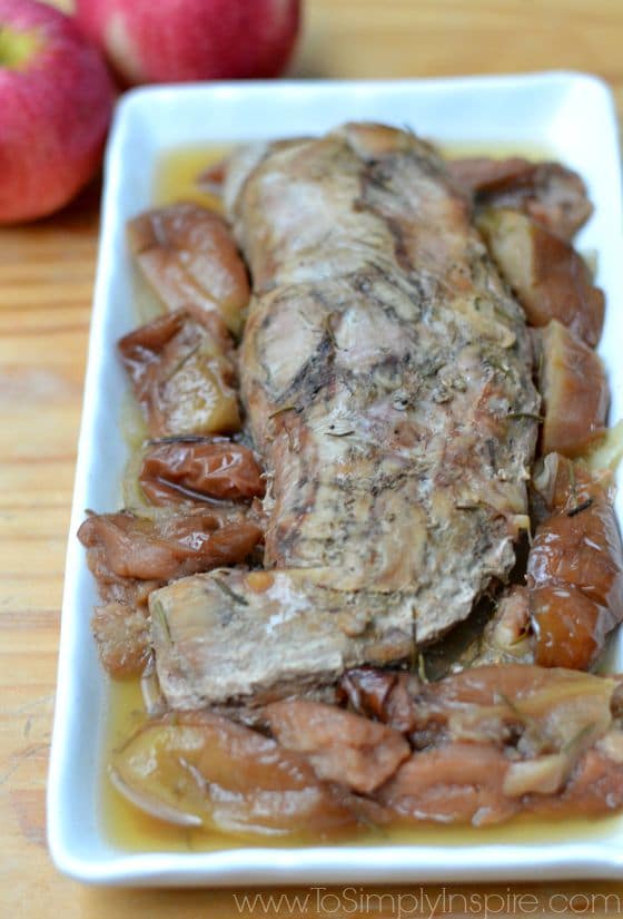 a closeup of cooked pork tenderloin surrounded by cooked apples on a white plate