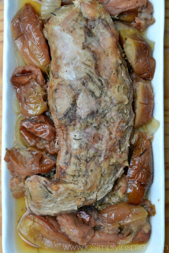 a white plate with a pork tenderloin topped with cooked apples and onions
