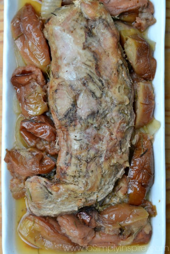 a white plate with a pork tenderloin topped with cooked apples and onions
