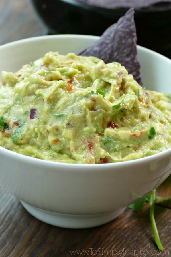 This easy Homemade Guacamole recipe is made with just a few all natural ingredients. Serve with your favorite chips or as the perfect topping on burrito bowls, chicken or fish. A close up of a bowl of Guacamole with a blue chip