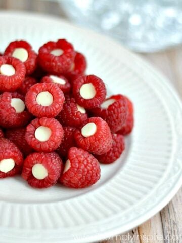 A close up of raspberries with white chocolate chip inside each on a white plate