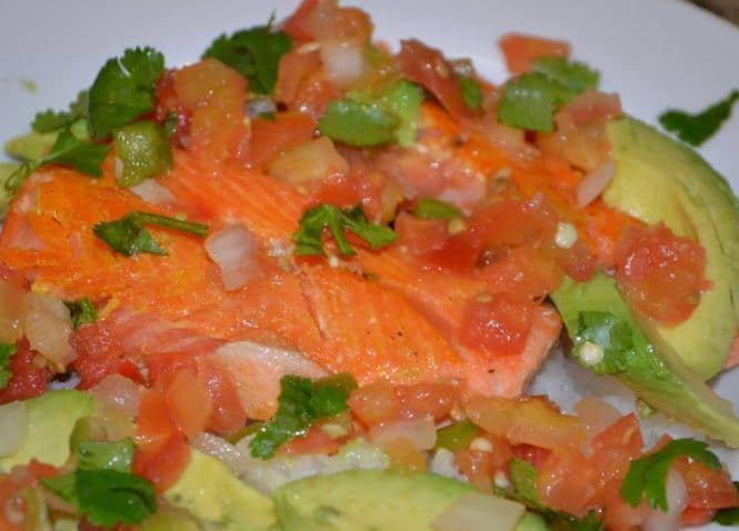 A close up of a plate of salmon over white rice covered in salsa