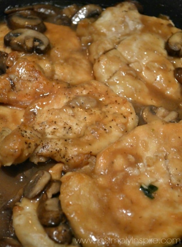A close up chicken breasts being cooked in a pan with mushrooms 