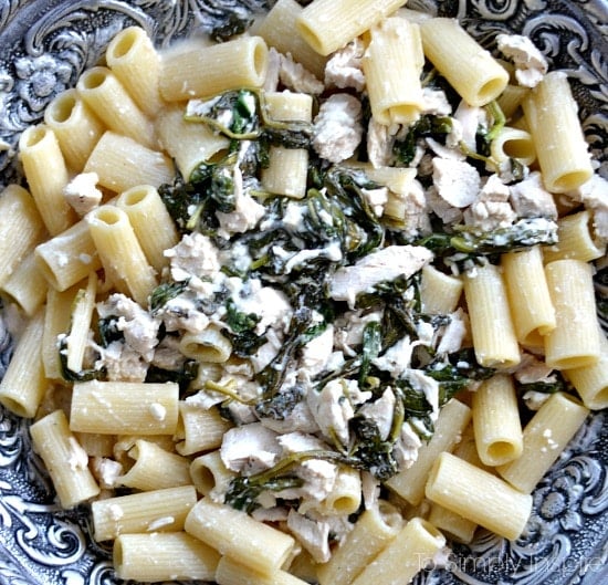 a bowl of penne pasta with chicken and cooked spinach mixture 