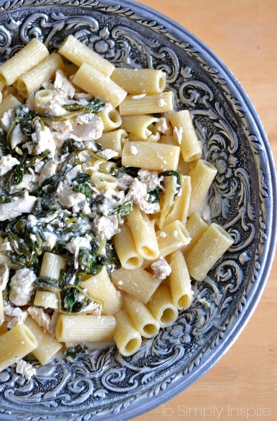 A big silver bowl with penne pasta topped with spinach and chicken mixture