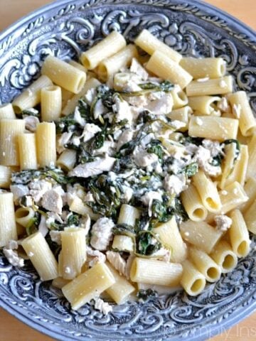 A big silver bowl with penne pasta topped with spinach and chicken mixture