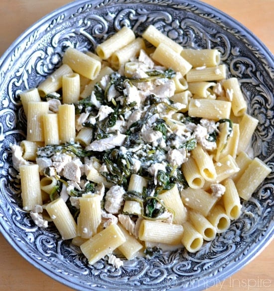 A bowl of pasta with spinach chicken feta sauce in a big silver serving bowl