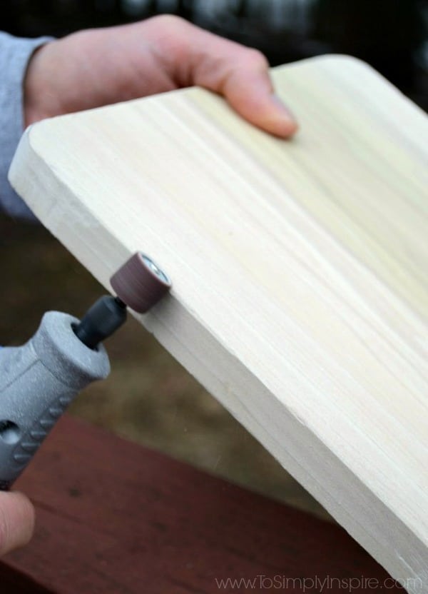 A close up of a hand holding a piece of wood and sanding the edges with a sanding tool