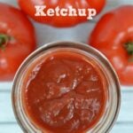 ketchup in a mason jar surrounded by three tomatoes