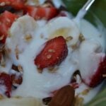 a green bowl of vanilla yogurt with strawberries and bananas