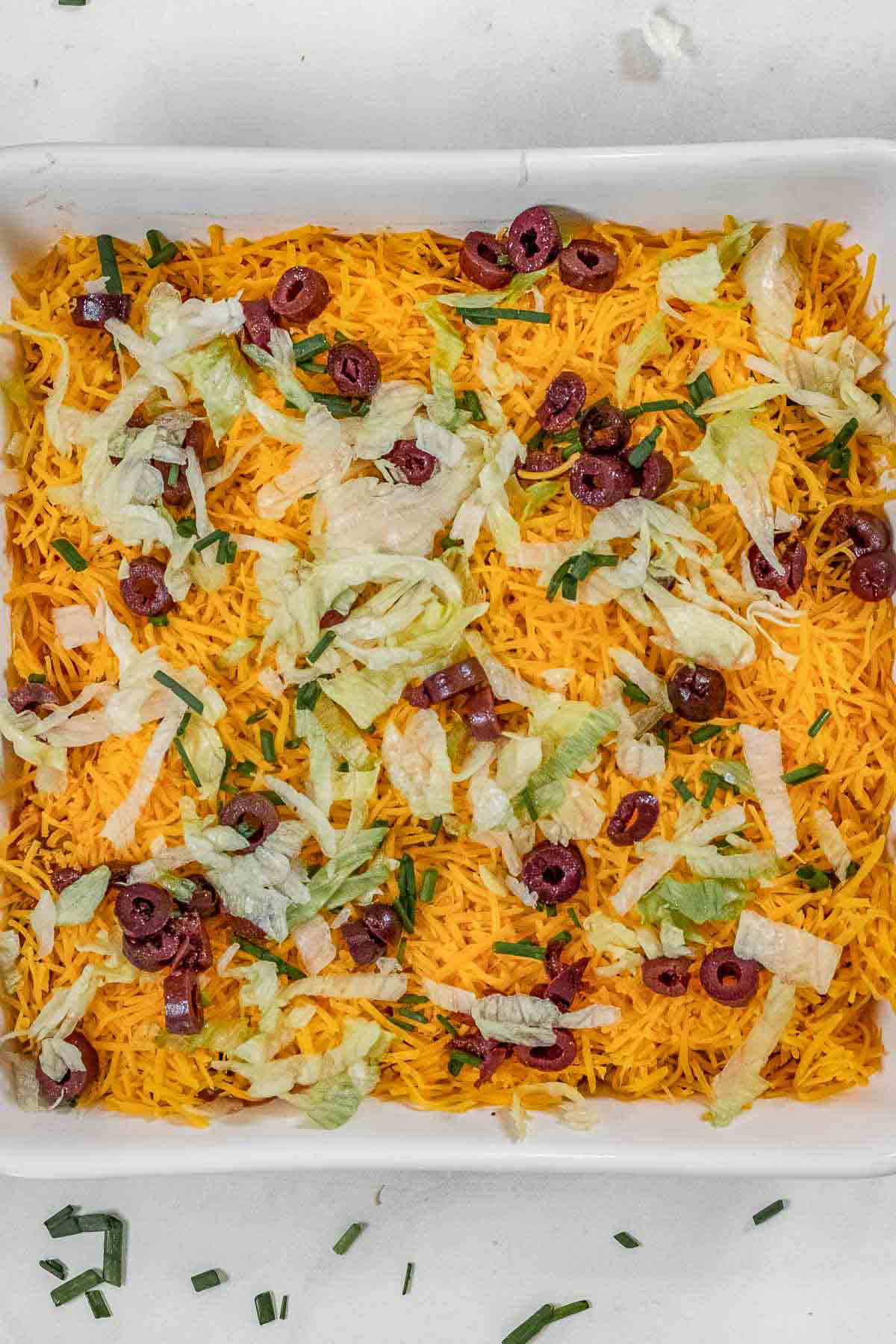 a wooden bowl of tortilla chips and a glass baking dish of taco dip topped with shredded cheese. 