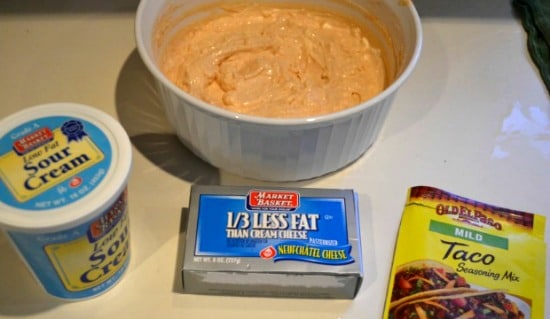 a white bowl with cream cheese taco dip mixture with a box of cream cheese, taco seasoning and carton of sour cream 