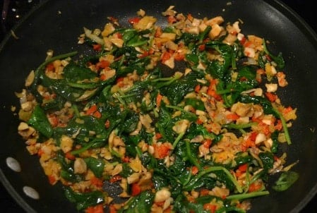 Closeup of cooked spinach, onions, mushrooms and red peppers in a black pan