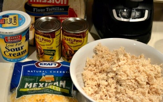 A close up of a bowl of shredded chicken, two cans of Enchilada sauce and a package of shredded cheese