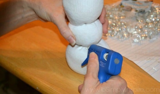 A close up of woman\'s hand glueing a white sock snowman craft