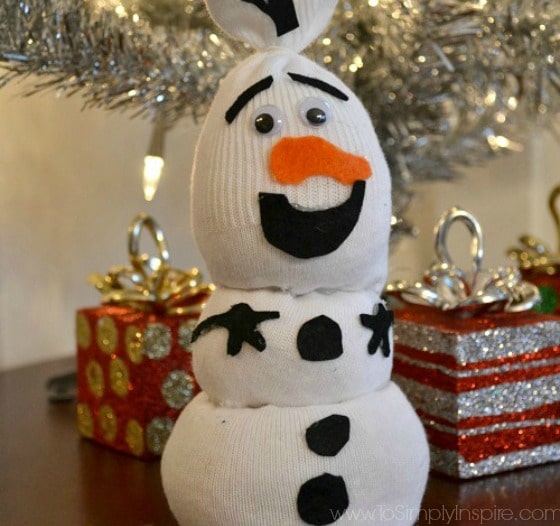 olaf sock snowman on a wood table in from of a small silver christmas tree