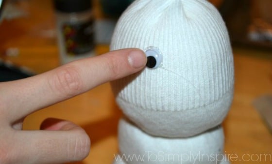 girls hand glueing a plastic eye on a sock snowman craft 