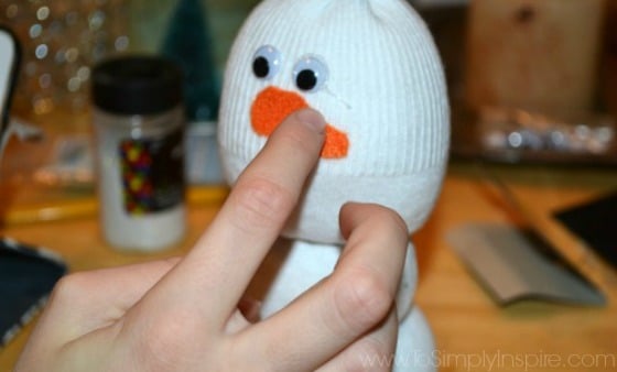 a girls hand placing a felt carrot nose on a sock snowman craft