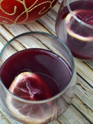 a stemless wine glass with red wine wassail and a lemon slice