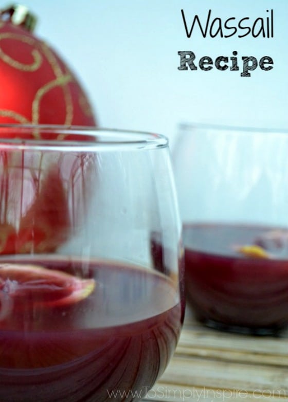 closeup of two stemless wine glasses with red wine wassail and a lemon slice with a big red christmas ornament 