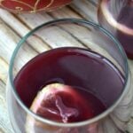 a stemless wine glass with red wine wassail and a lemon slice