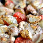 A close up of roasted Chicken thighs, tomatoes, potatoes and onions