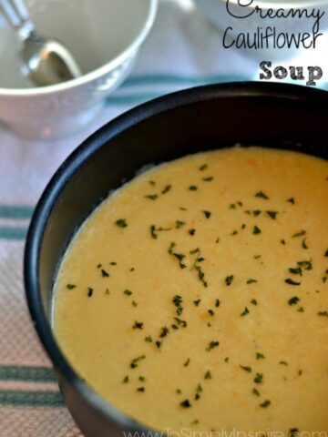 A black pot of creamy Cauliflower soup topped with parsley