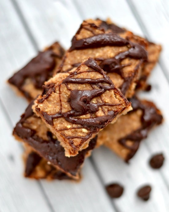 A close up of banana bars drizzled with chocolate on a grey wood table