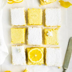 several lemon bars on white parchment paper, some topped with powdered sugar