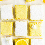 nine lemon bars on a white table some topped with powdered sugar