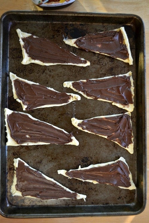 Uncooked crescent roll dough with nutella spread each piece.