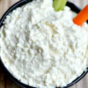 closeup of a bowl of ranch cottage cheese dip with a piece of celery and carrot dipped in