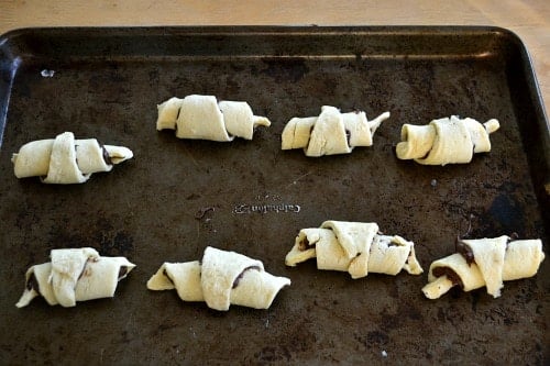 uncooked crescent rolls rolled up and placed on a baking sheet