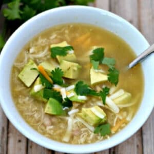 white bowlful of white chicken chili topped with avocado and cilantro