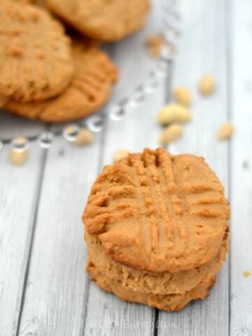 a stack of peanut butter cookies with a plateful in the background