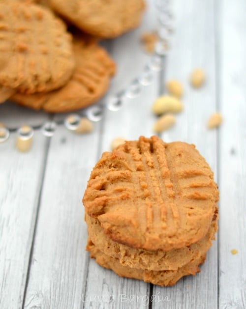 a stack of 3 peanut butter cookies surrounded by peanuts