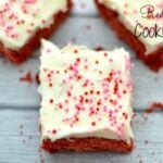 Three red velvet cake cookie bars topped with cream cheese frosting and sprinkles