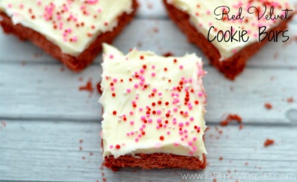 a closeup of three red velvet cake cookie bars topped with cream cheese frosting and sprinkles