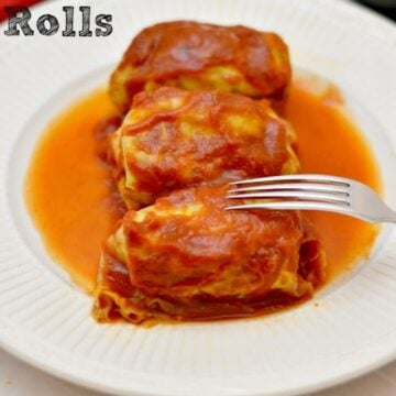 A white plate of three cabbage rolls topped with tomato sauce
