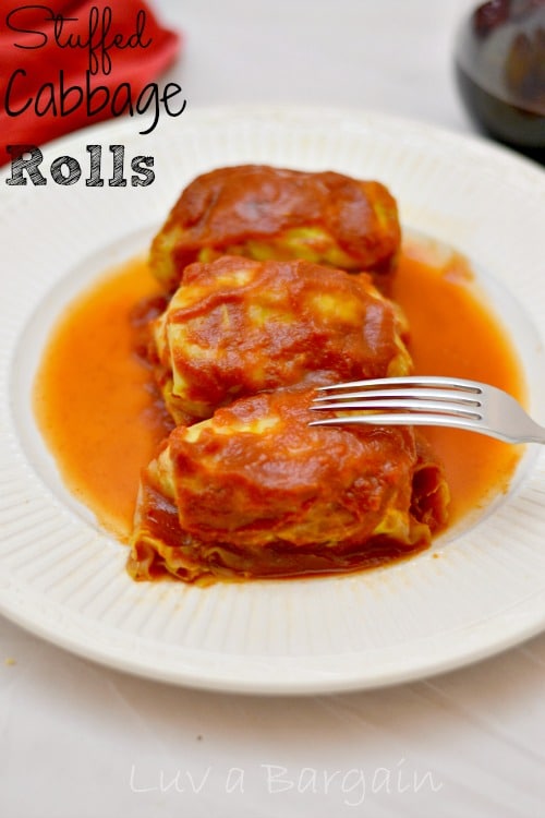 A white plate of three cabbage rolls topped with tomato sauce