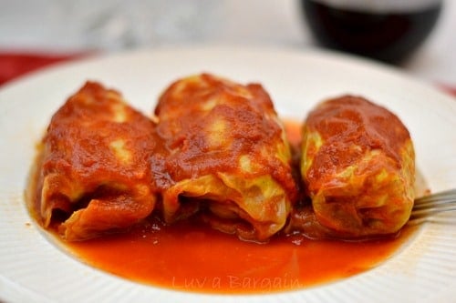three cabbage rolls topped with tomato sauce on a white plate