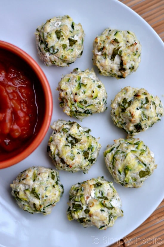 eight turkey zucchini meatballs on a white plate with a small bowlful of salsa